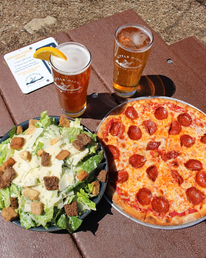 A pepperoni pizza, Caesar salad, and two beers from Little Miami Brewing Company on an outdoor table, with a slice of lemon in one of the beers.